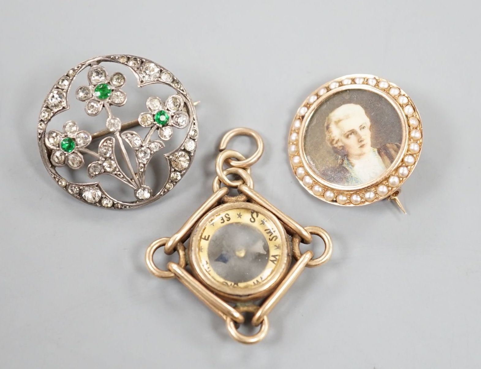 An American 10k yellow metal compass pendant, 29mm, gross 7.1 grams, a 585 and split pearl set circular portrait brooch, gross 4 grams and a two colour paste set brooch.